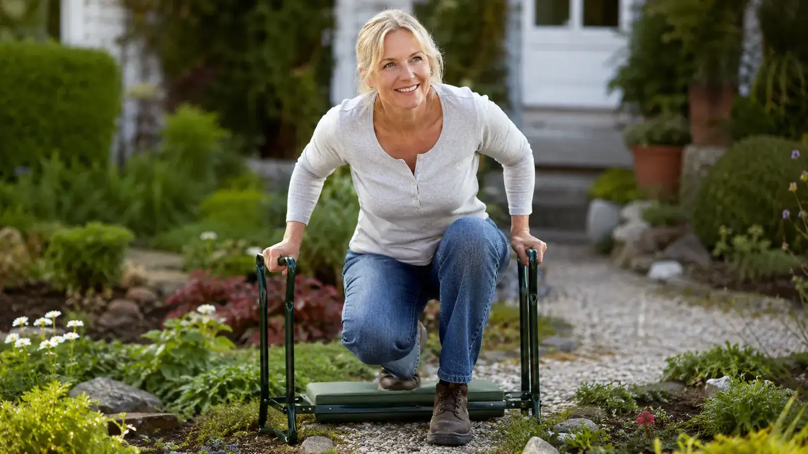 Happy home gardener sitting on a garden bench kneeler, trowel in hand, relaxed posture among tomato plants