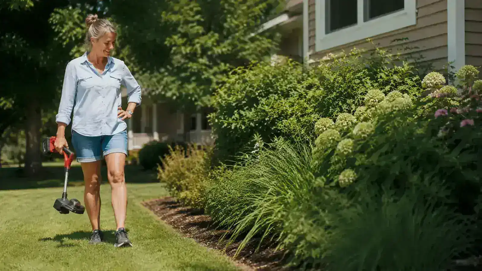 Woman sitting on porch steps with an iced tea, looking out at a tidy garden bed and lawn in late afternoon